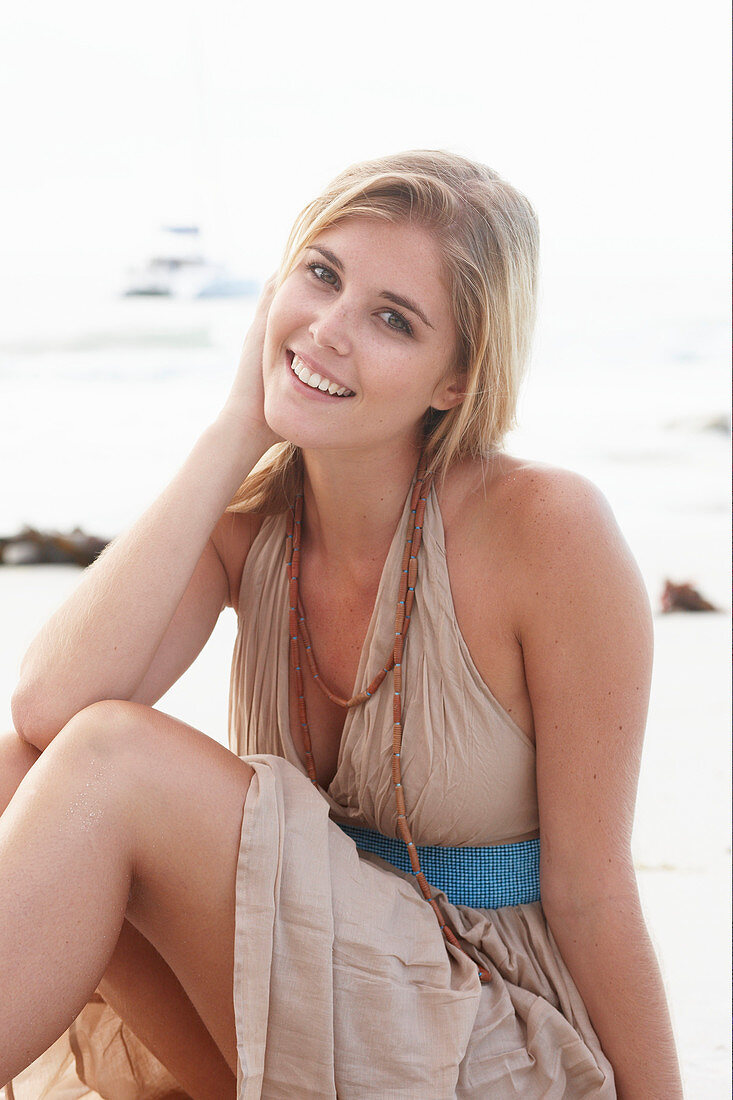 A blonde woman on a beach wearing a beige summer dress