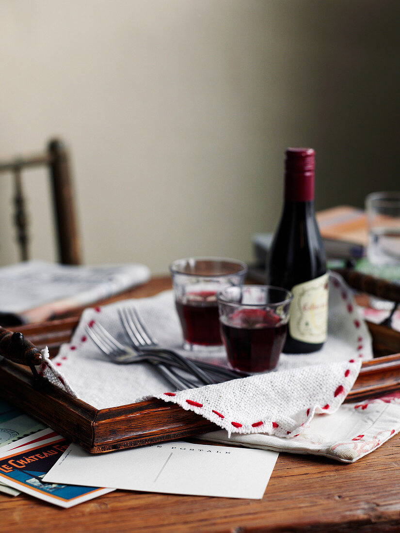 A bottle of red wine and red wine glasses on a wooden tray on a wooden table