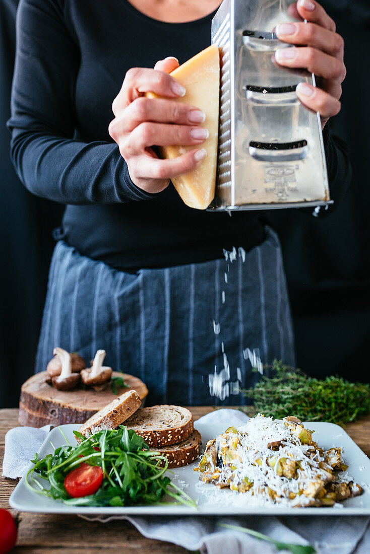 Person grating parmesan on top of the scrambled eggs made with mushrooms