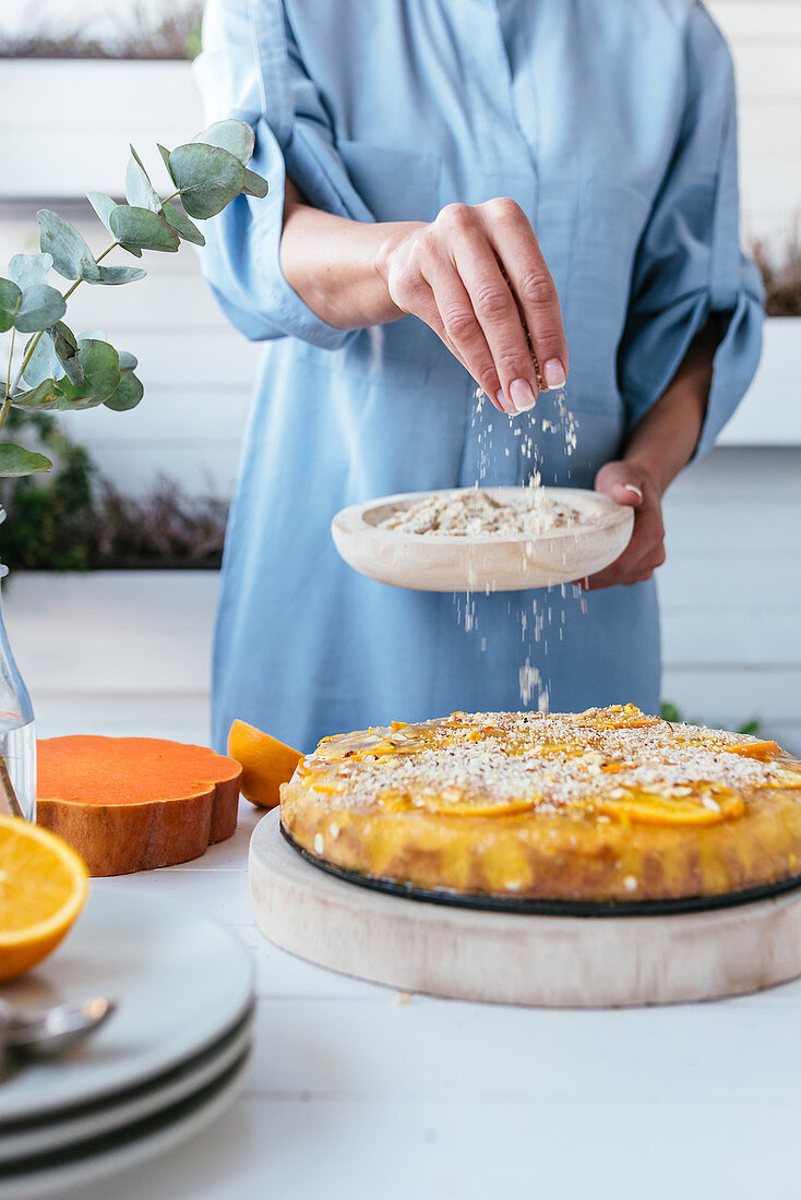 Person covering pumpkin and oranges tart with grinded walnuts