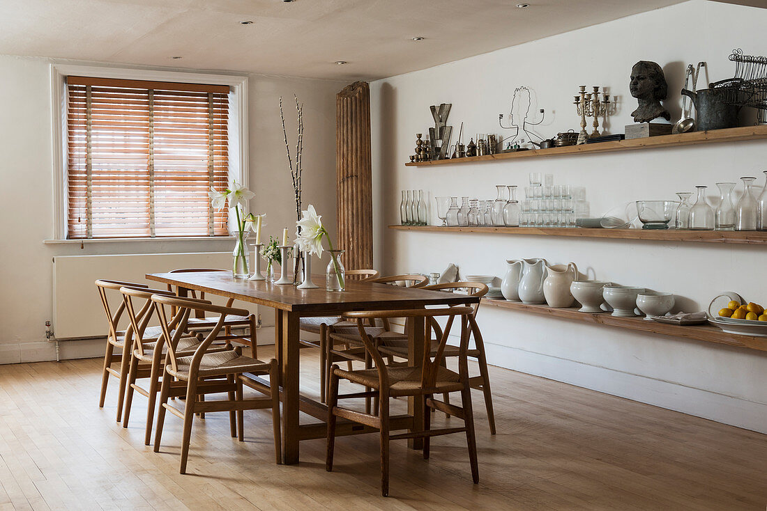 Large farmhouse dining table with wooden chairs in stylish dining room with open shelving