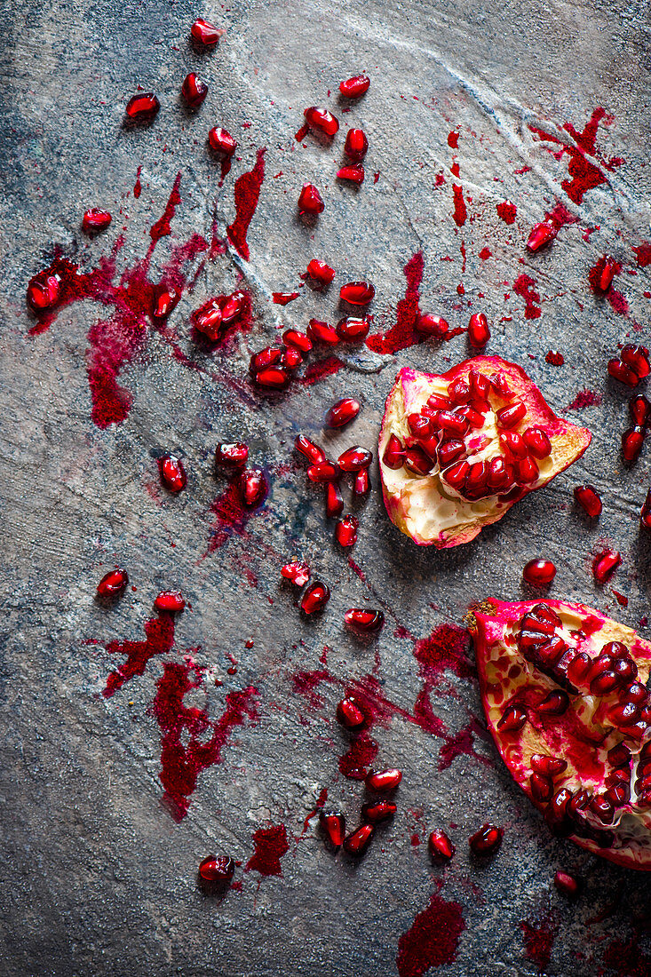 Pieces of pomegranate and pomegranate seeds on a grey surface