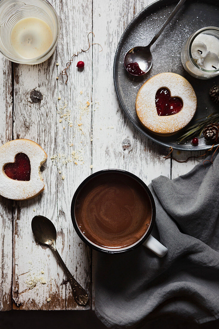 A cup of hot chocolate and some biscuits with jam on the table