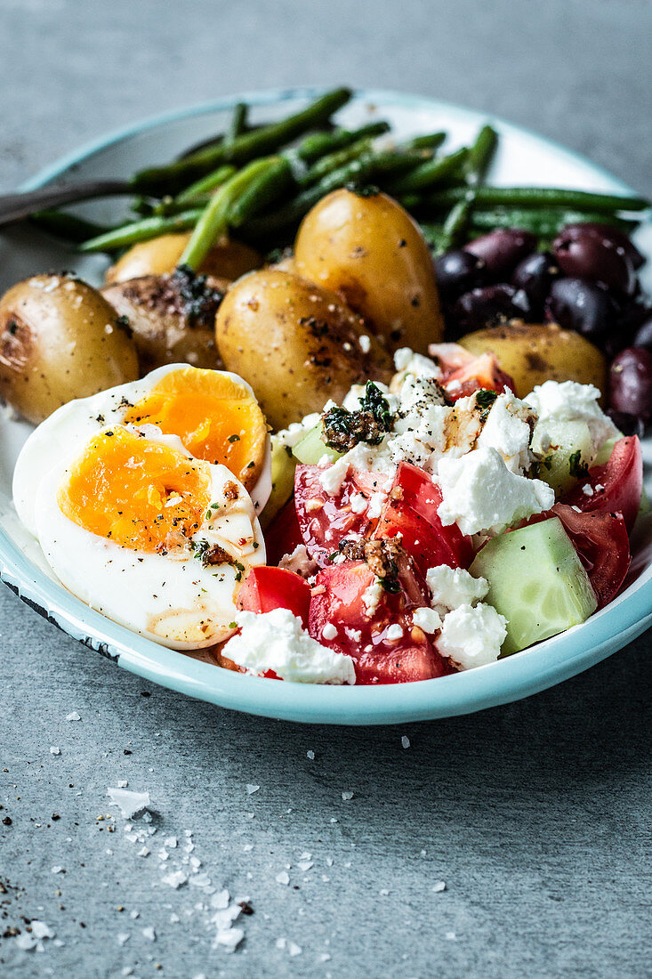 Antipasti-Platte mit Bohnen, Kartoffeln, Oliven, Ei und griechischem Salat