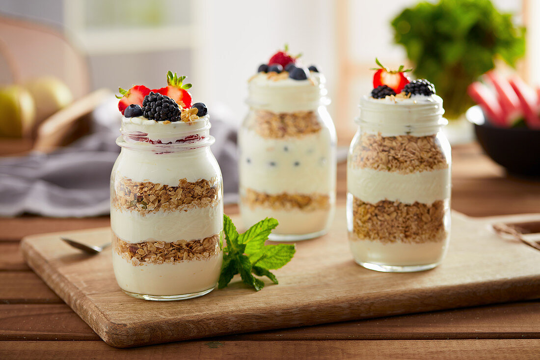 Delicious breakfast served in glass jars with layered yogurt and granola under topping of fresh summer berries
