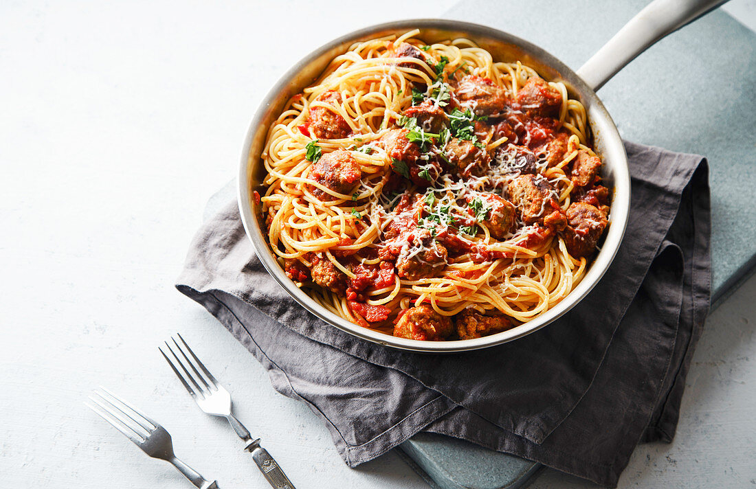 Spaghetti with meatballs, tomato sauce, parsley and cheese served in a pan