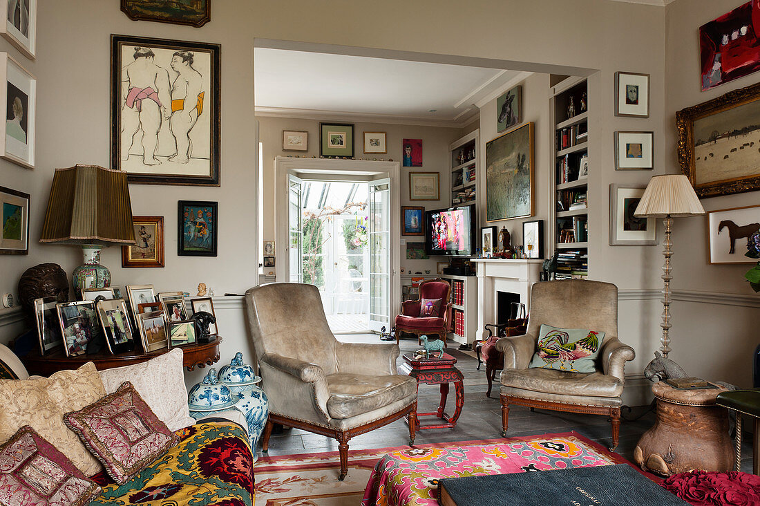 Eklektisch eingerichtetes Wohnzimmer mit verschiedenen Kunstwerken und cremefarbenen Ledersesseln