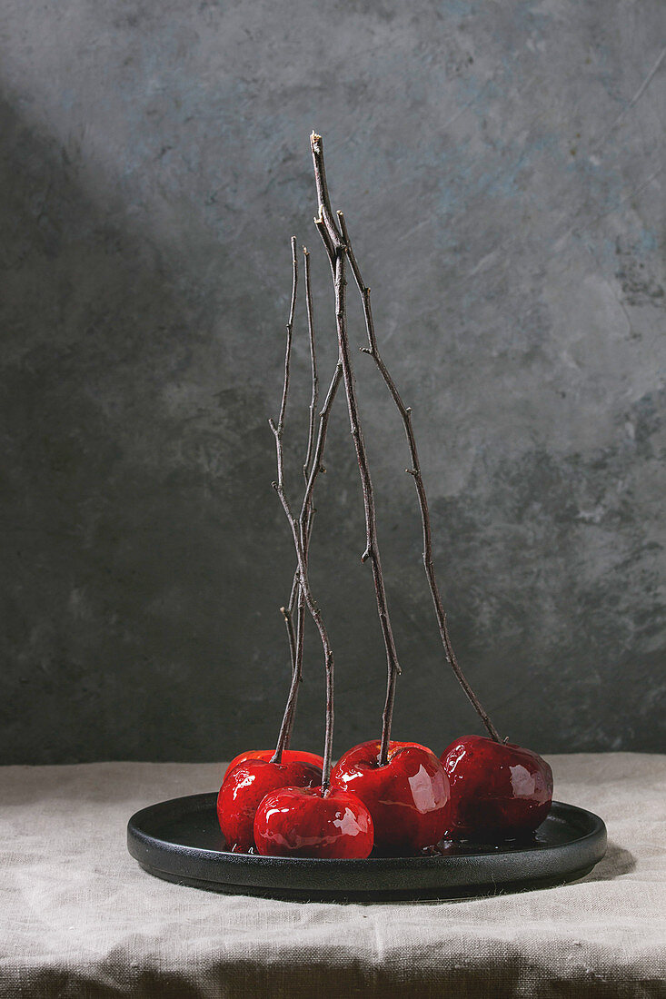 Red caramel apples sweet autumn or Christmas dessert served with branches in black ceramic plate