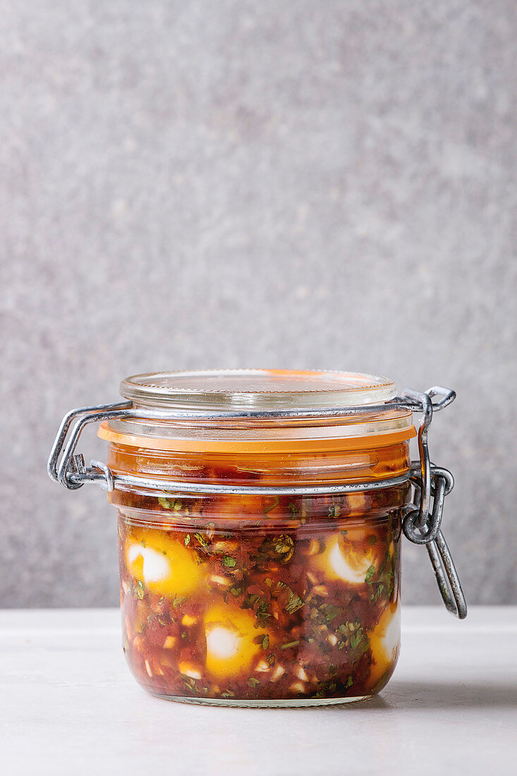 Jar with homemade pickled marinated quail eggs in tomato and olive oil sauce with anchovies and fresh parsley