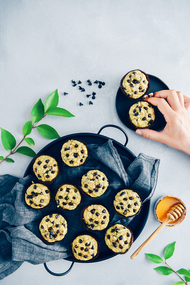 A hand grabbing a chocolate chip zucchini muffin from a black ceramic plate