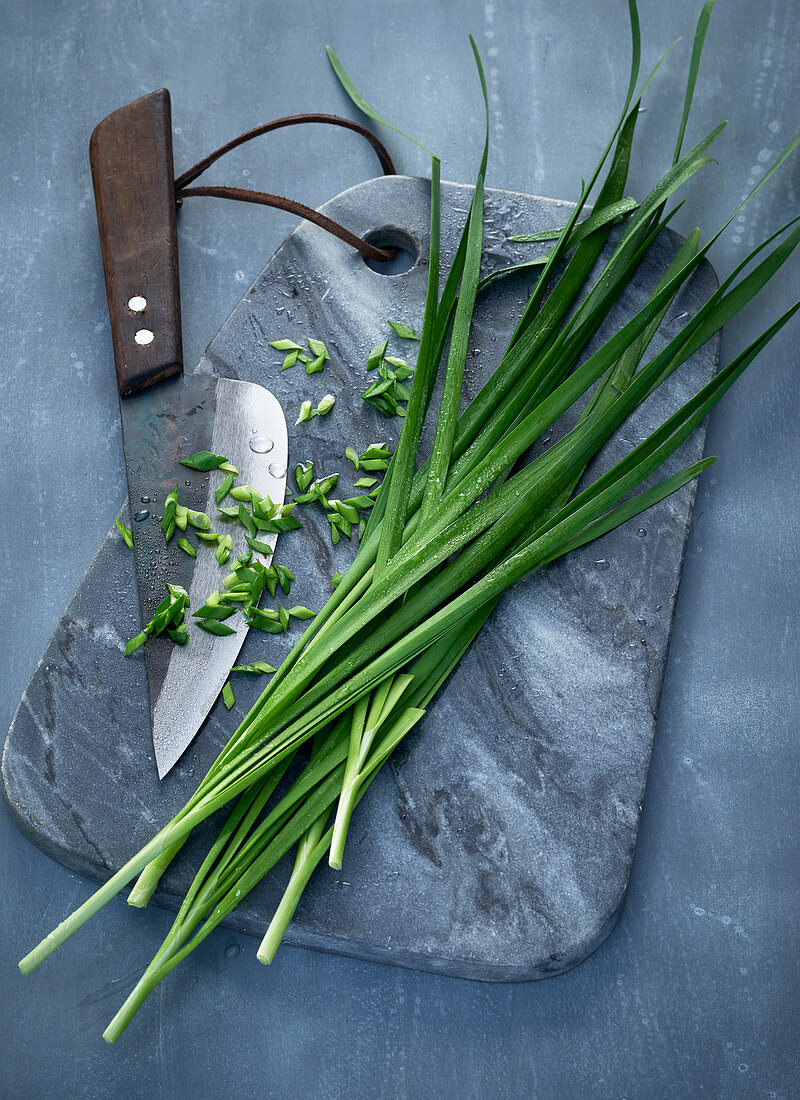 Asiatischer Schnittknoblauch auf grauem Mamorbrett mit Messer