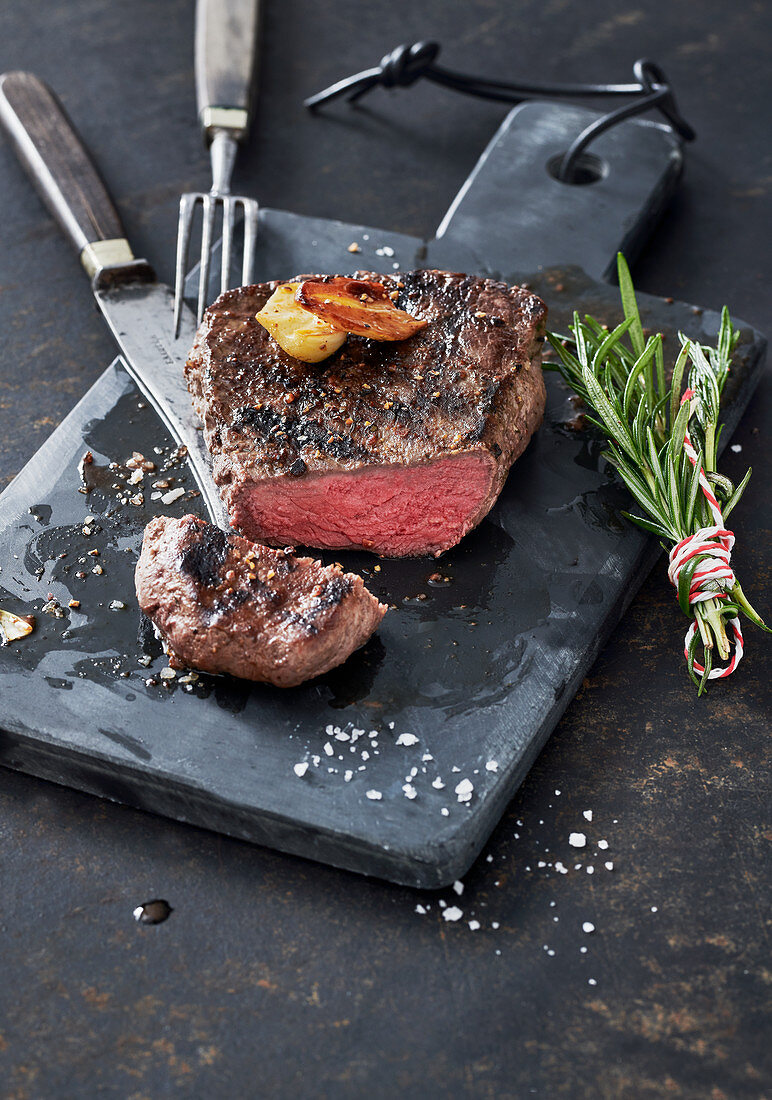 Grilled steak with garlic and a bundle of rosemary on a slate board