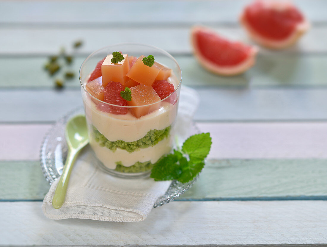 Vegan layered dessert in a glass with matcha and pistachio sponge, soya cream and pink grapefruit