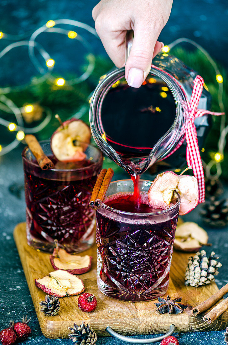 Girl pours Christmas mulled wine with dried apples from a carafe in crystal glasses