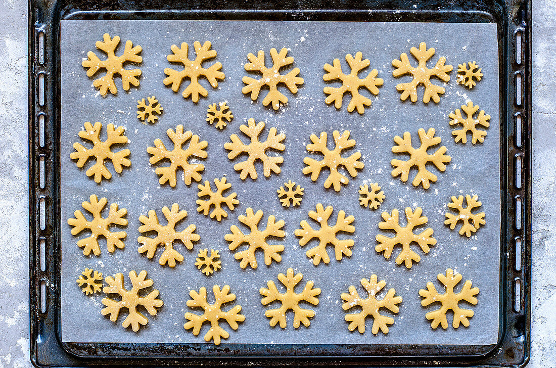 Gingerbread dough cut in the form of snowflakes on parchment and deco before baking