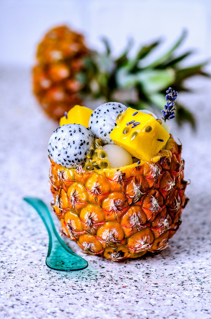 Fruit salad with various tropical fruits in a pineapple with blue transparent spoon