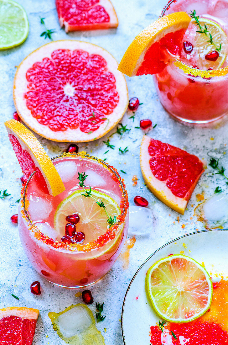 Grapefruit mocktail with color sugar, ice decorated with grapefruit slices, pomegranate seeds and thyme sprigs