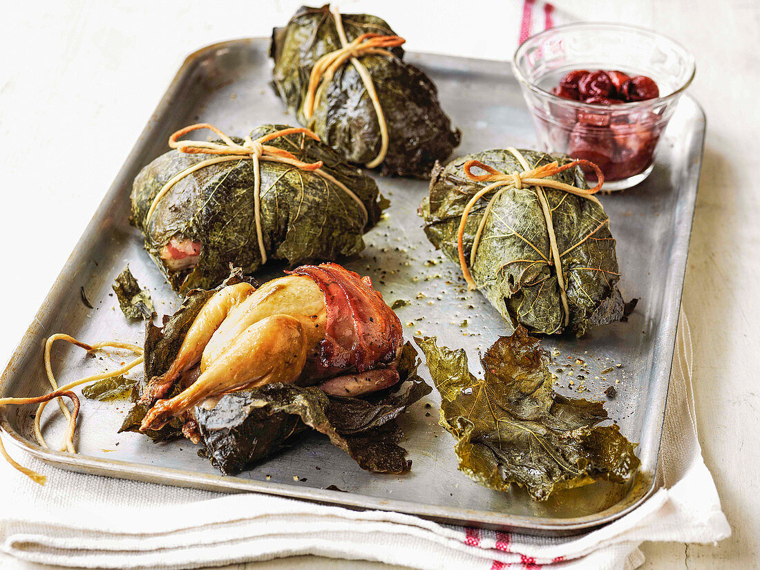 Quail in vine leaves and wrapped in pancetta with red grape compote on a roasting tray
