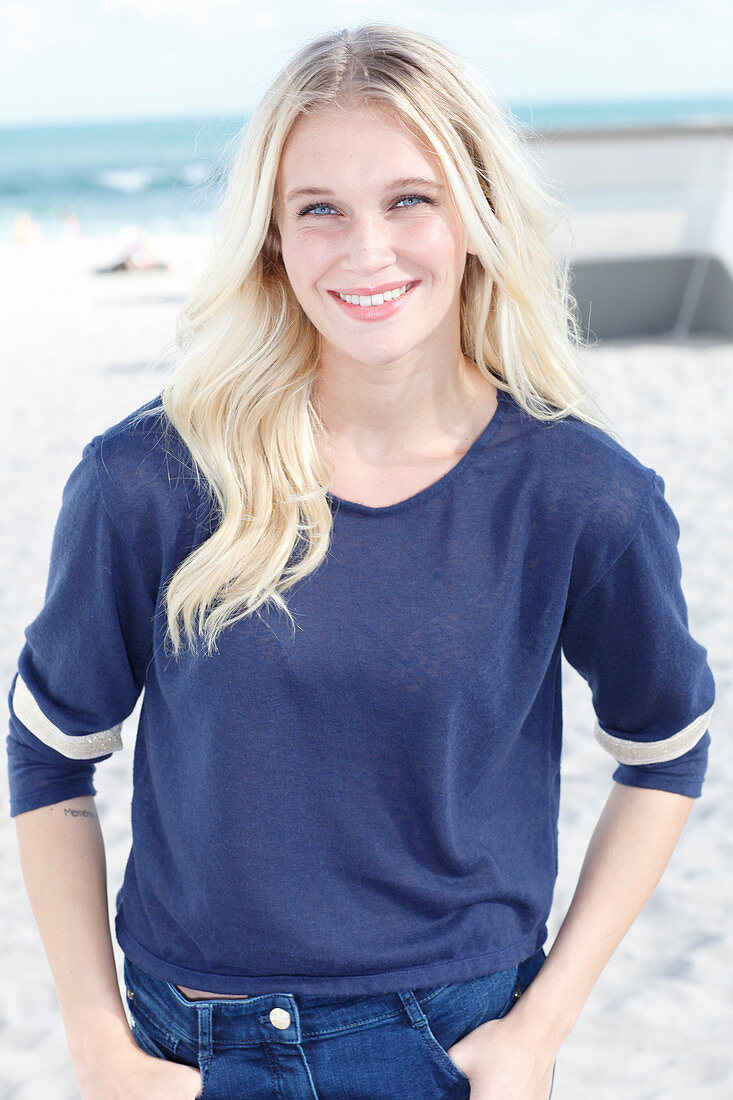 A young blonde woman on a beach wearing a long-sleeved blue shirt