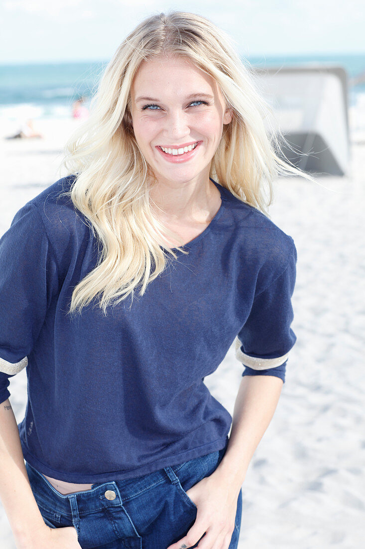 Junge blonde Frau in blauem Langarmshirt am Strand