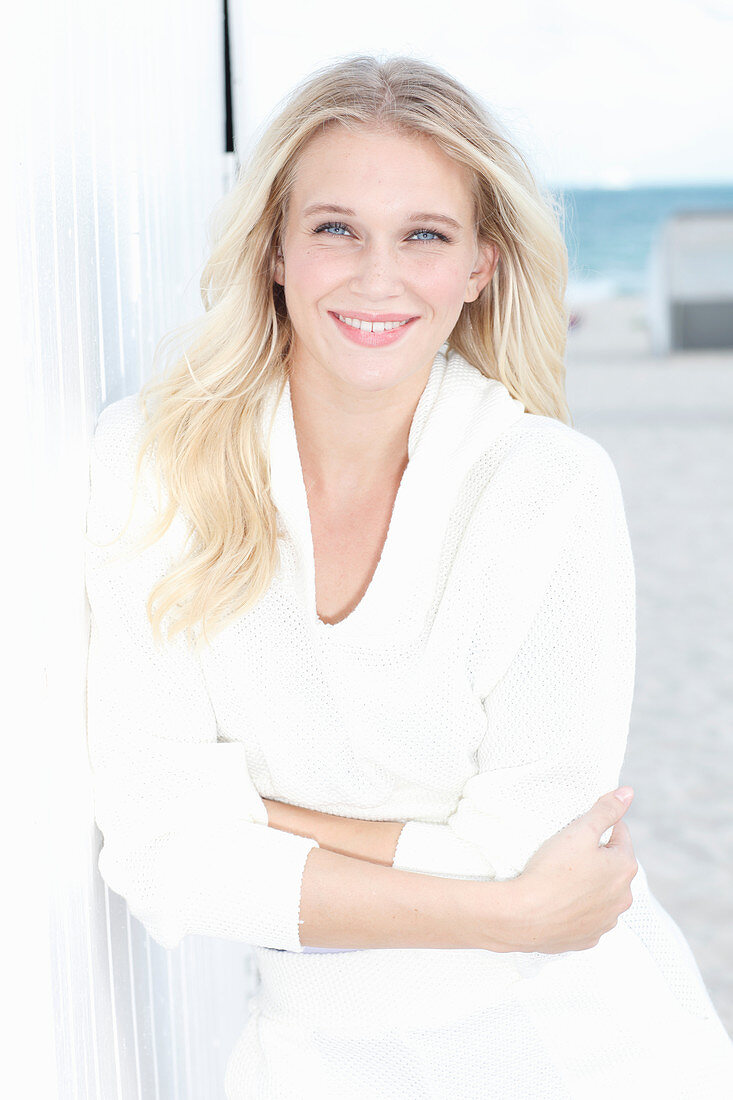 A young blonde woman on a beach wearing a white top