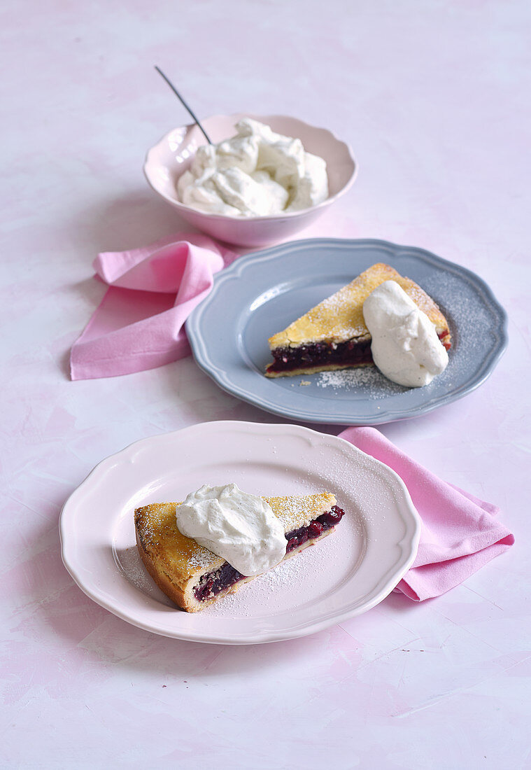 Two pieces of cherry vanilla pie with cream on plates