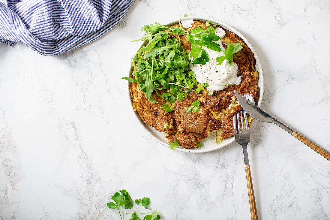 Tortilla omelette with sliced potatoes and herbs on marble table