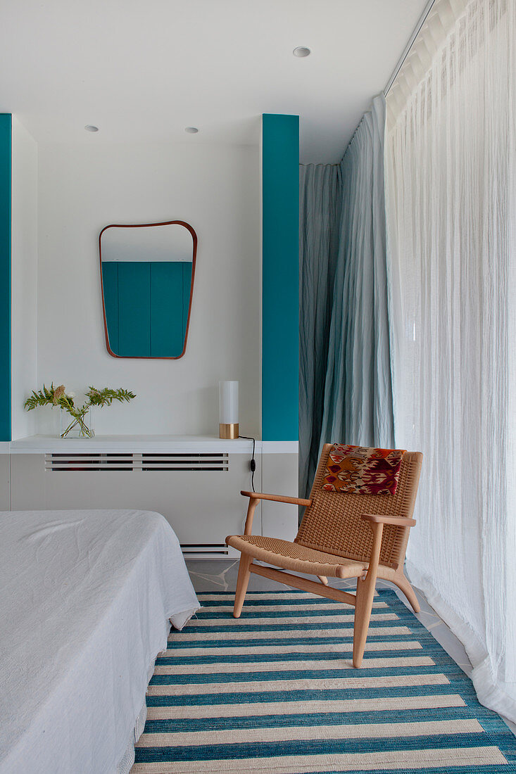 Weißes Schlafzimmer mit türkisfarbenen Akzenten, Stuhl vor Fenster mit bodenlangem Vorhang