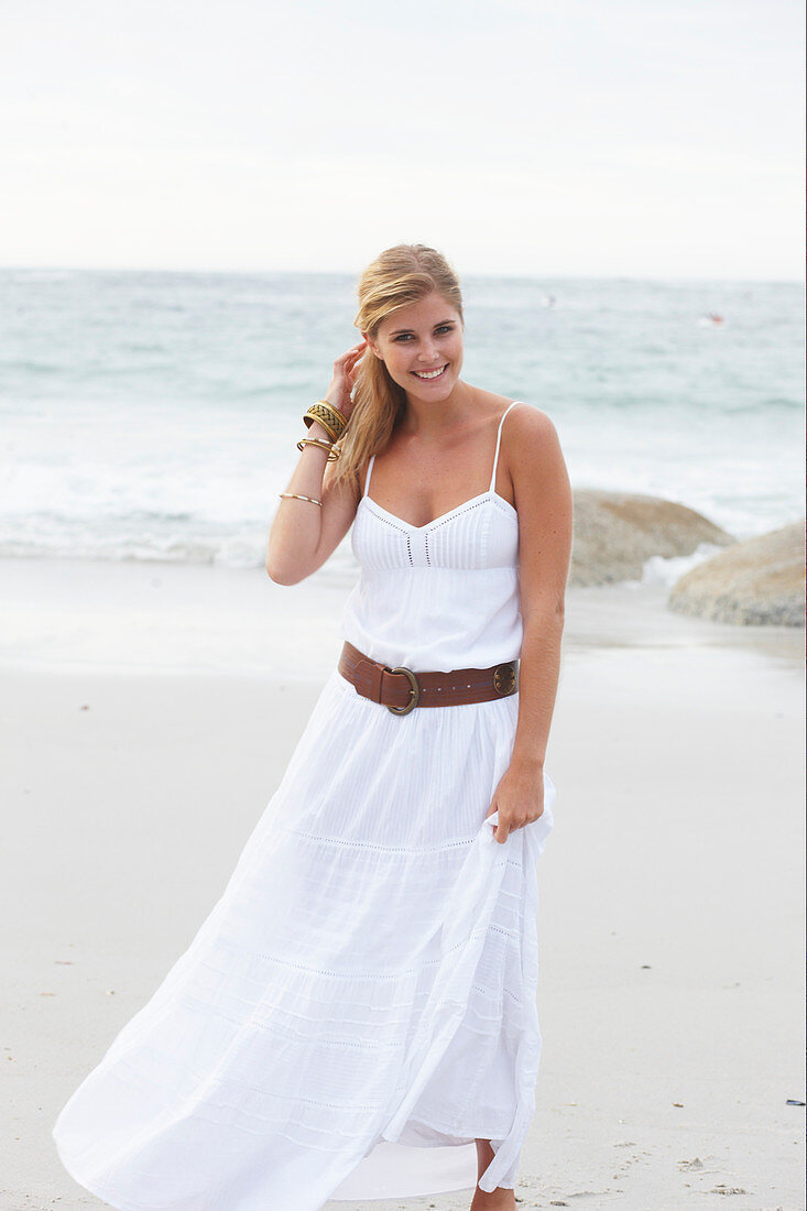 A blonde woman by the sea wearing a white summer dress