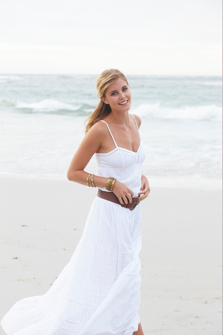 A blonde woman by the sea wearing a white summer dress