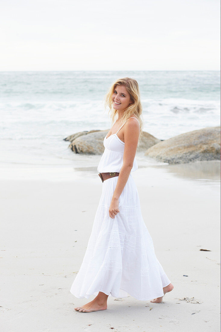 A blonde woman by the sea wearing a white summer dress