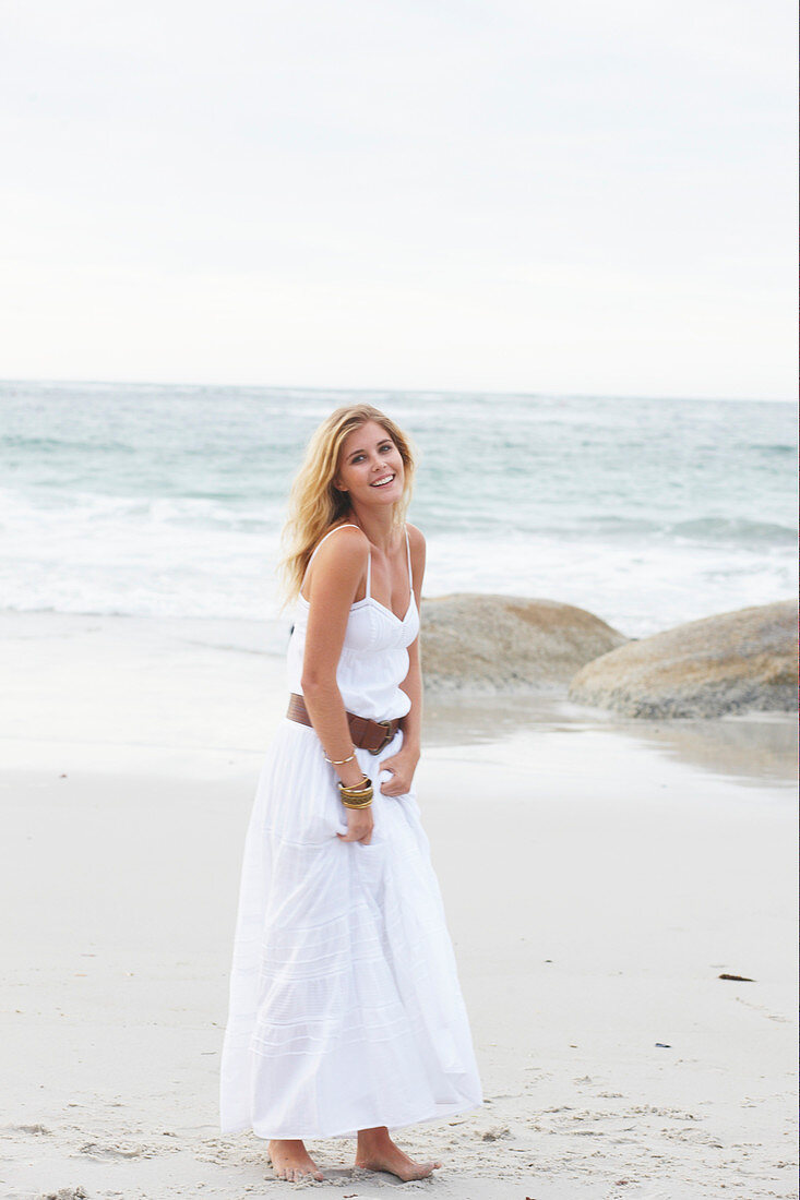 A blonde woman by the sea wearing a white summer dress