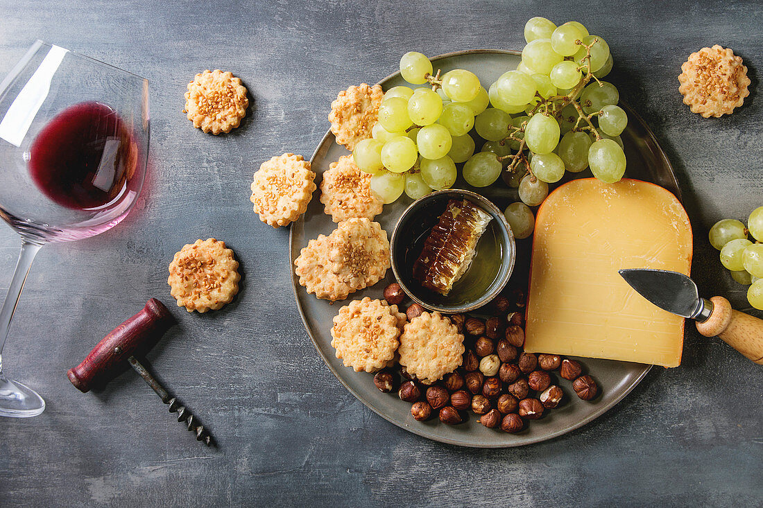 Käsecracker serviert mit Trauben, Käse, Nüssen, Honig und Rotwein (Aufsicht)