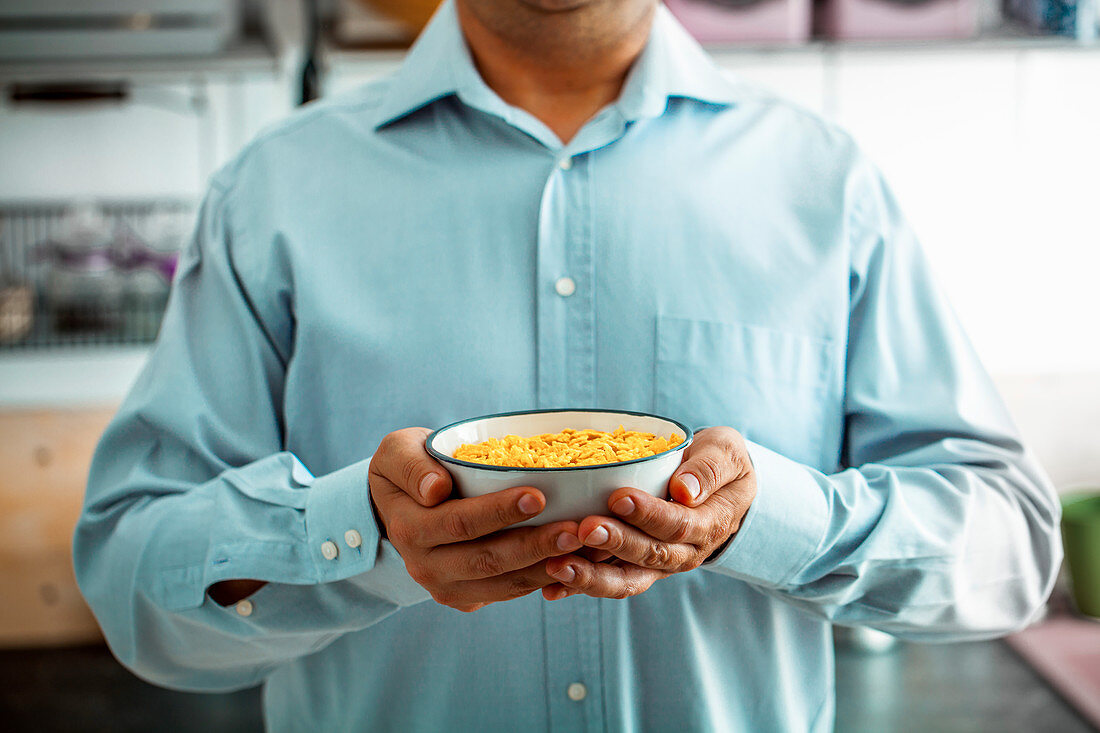 Mann hält eine Schale Cerealien mit Obst, Joghurt und Samen