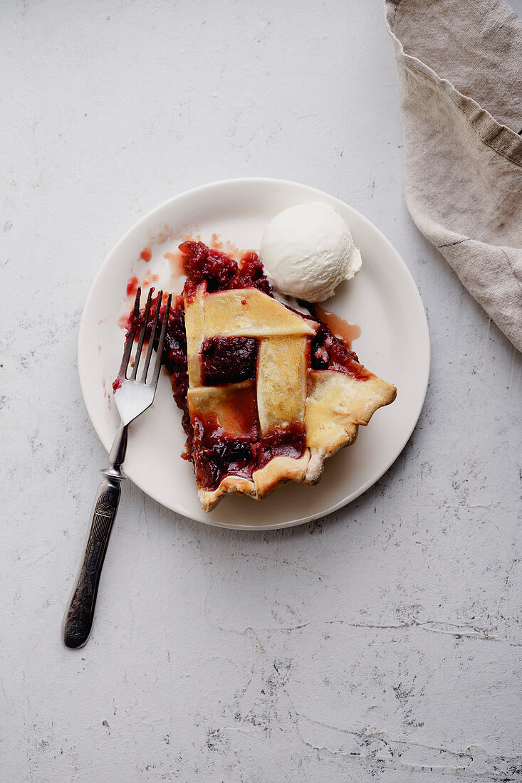 A slice of berry pie on a white plate served with a scoop of ice-cream