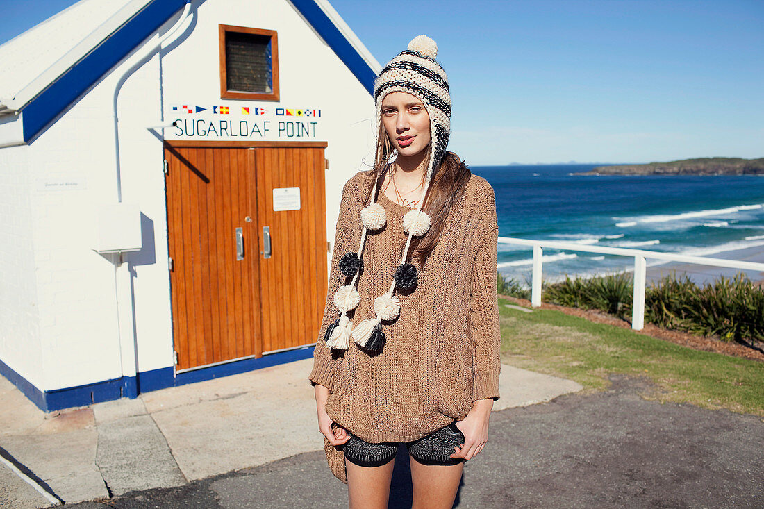 A young brunette woman wearing a knitted jumper, shorts and a hat