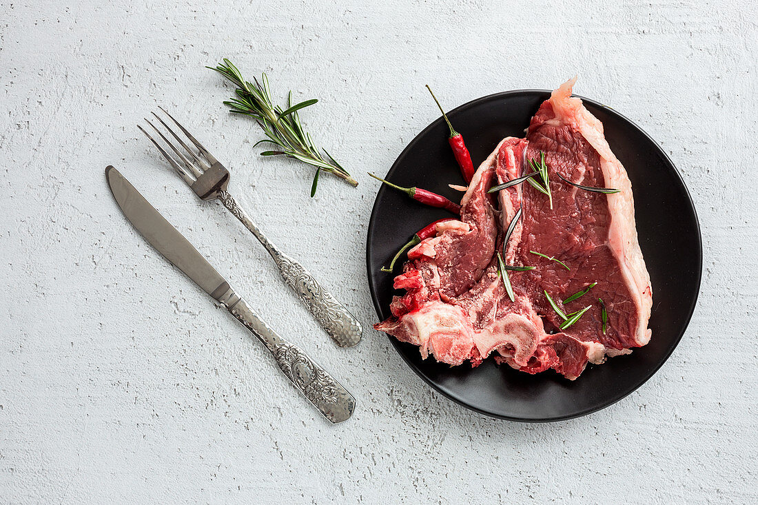 Raw beef steak with rosemary and chilli peppers