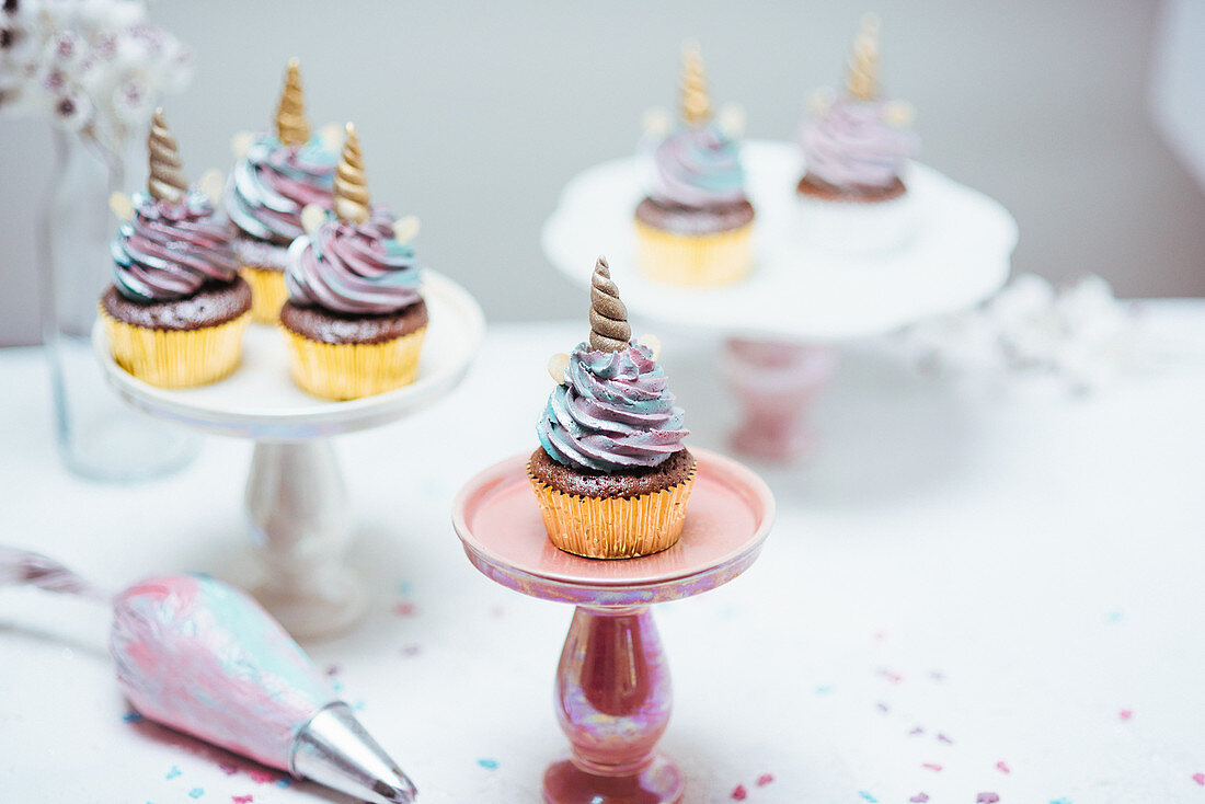 Muffins mit pastellfarbener Cremehaube verziert mit Einhorn-Horn