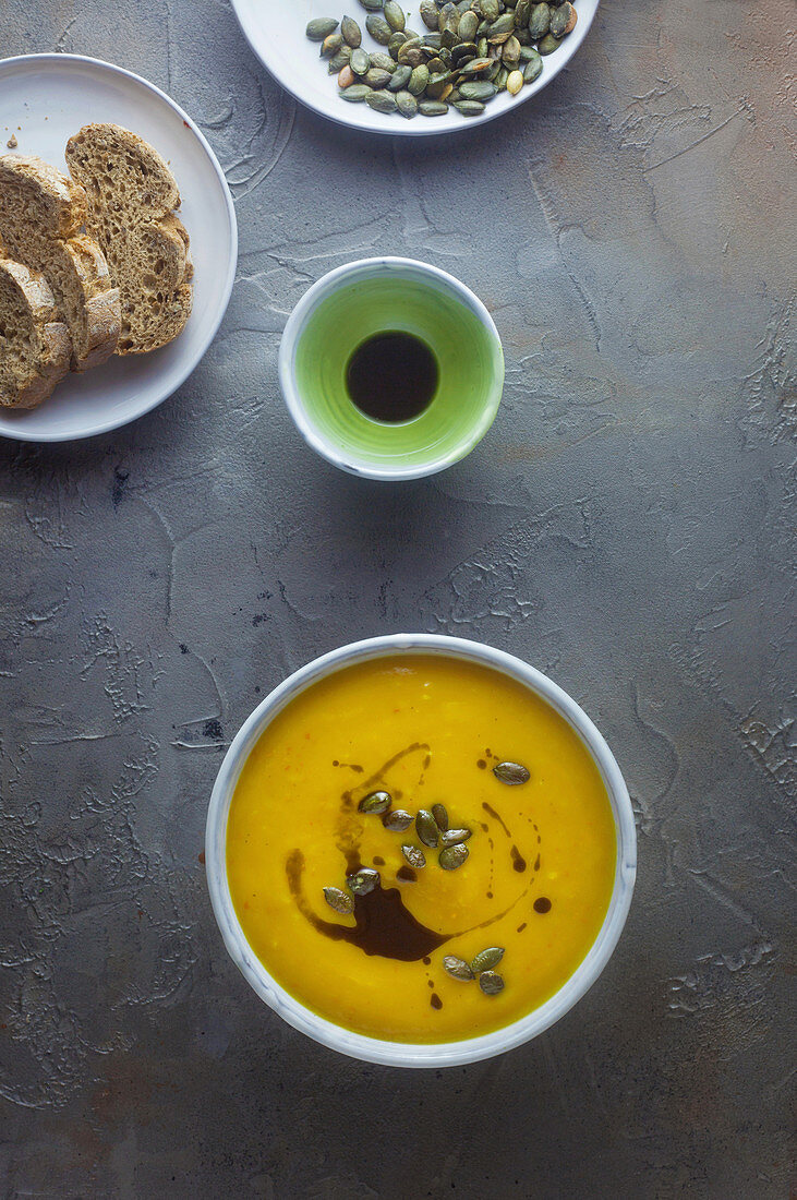 Cream of pumpkin soup with pumpkin seeds and pumpkin seed oil on a grey surface