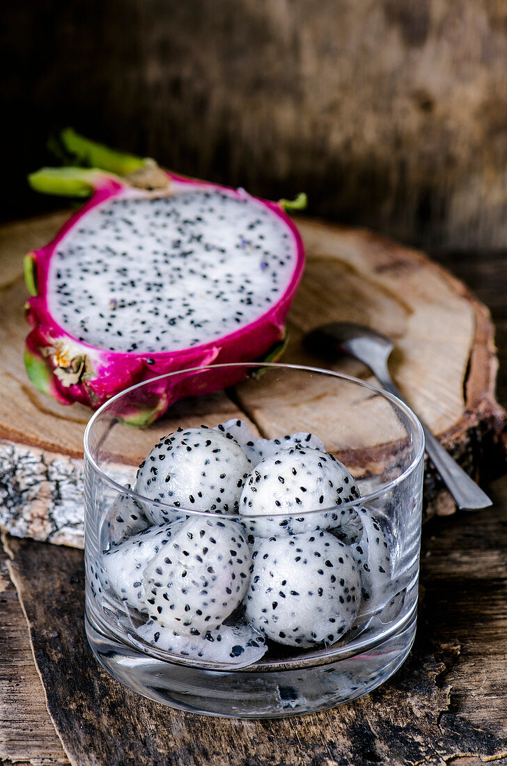 Balls cut with a special spoon from a Dragon fruit in a glass and half of fruit in the background