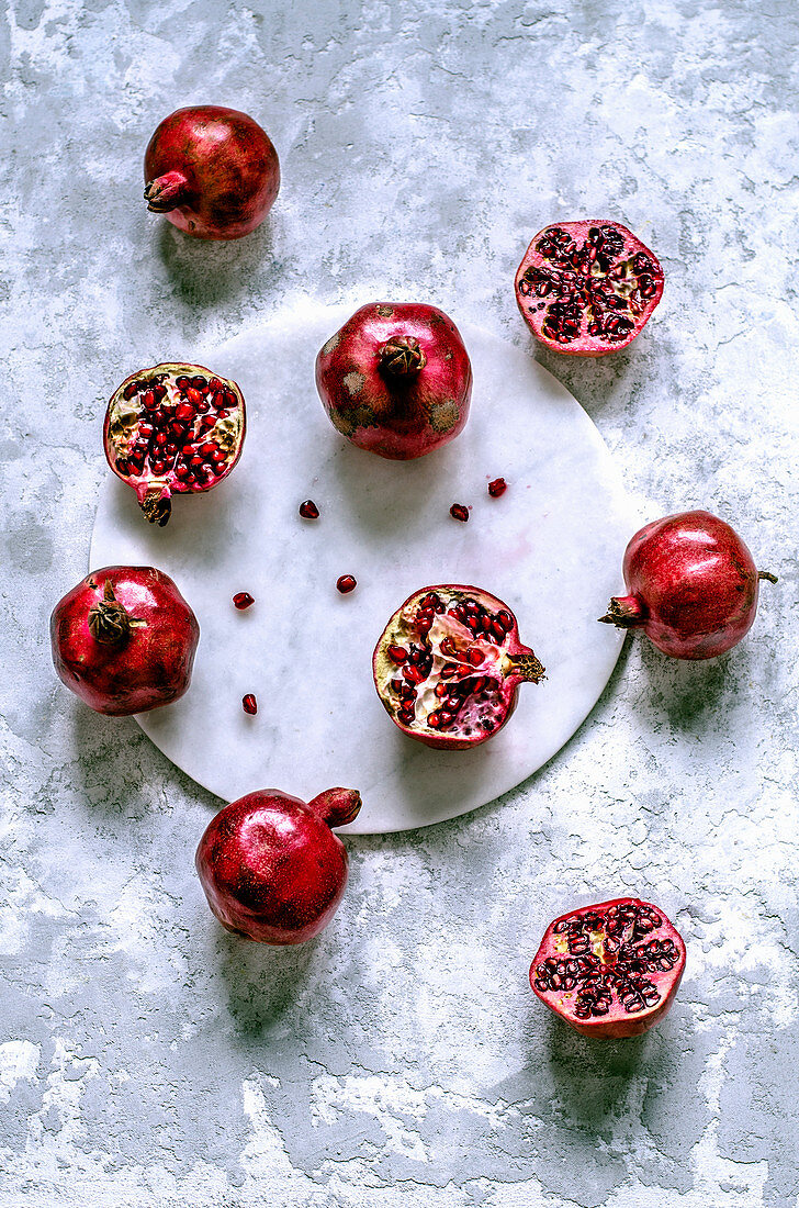 Fresh pomegranates whole and cut with scattered grains on a marble tray