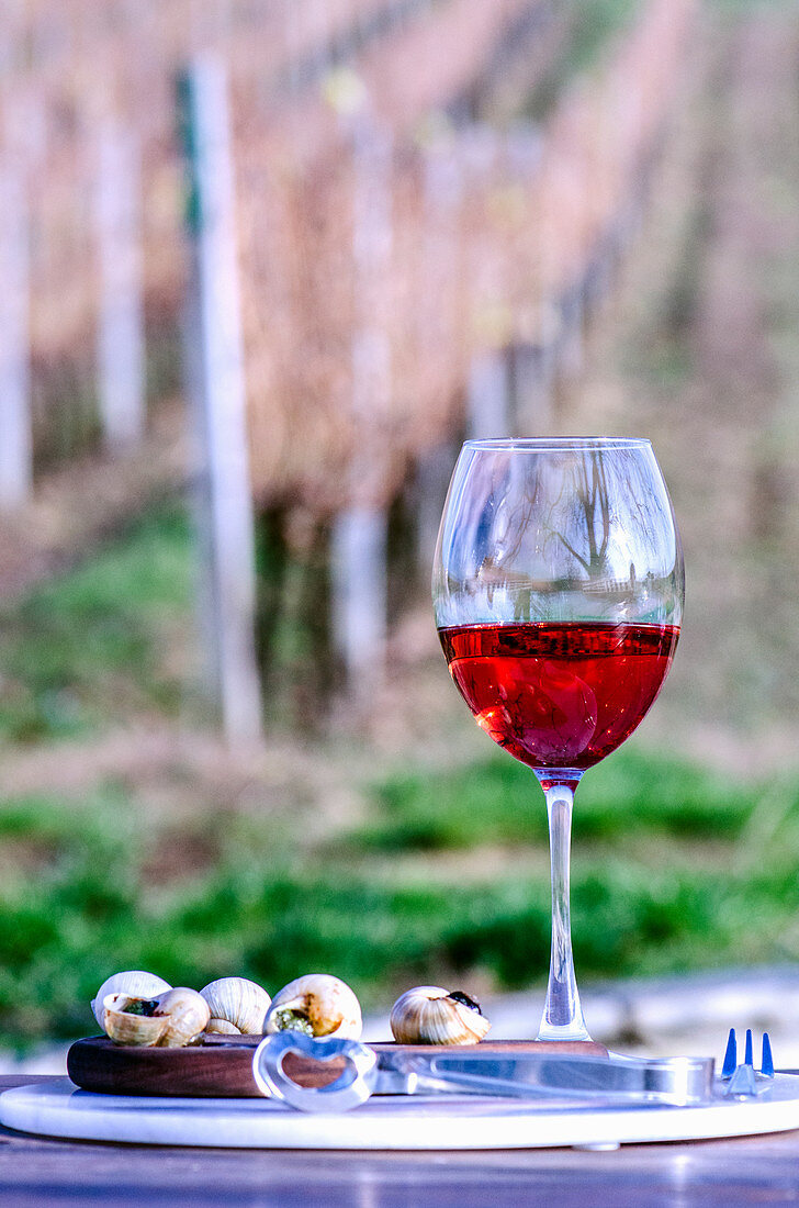 Ein Glas Rosewein serviert mit gefüllten Schnecken auf Tisch am Weinberg