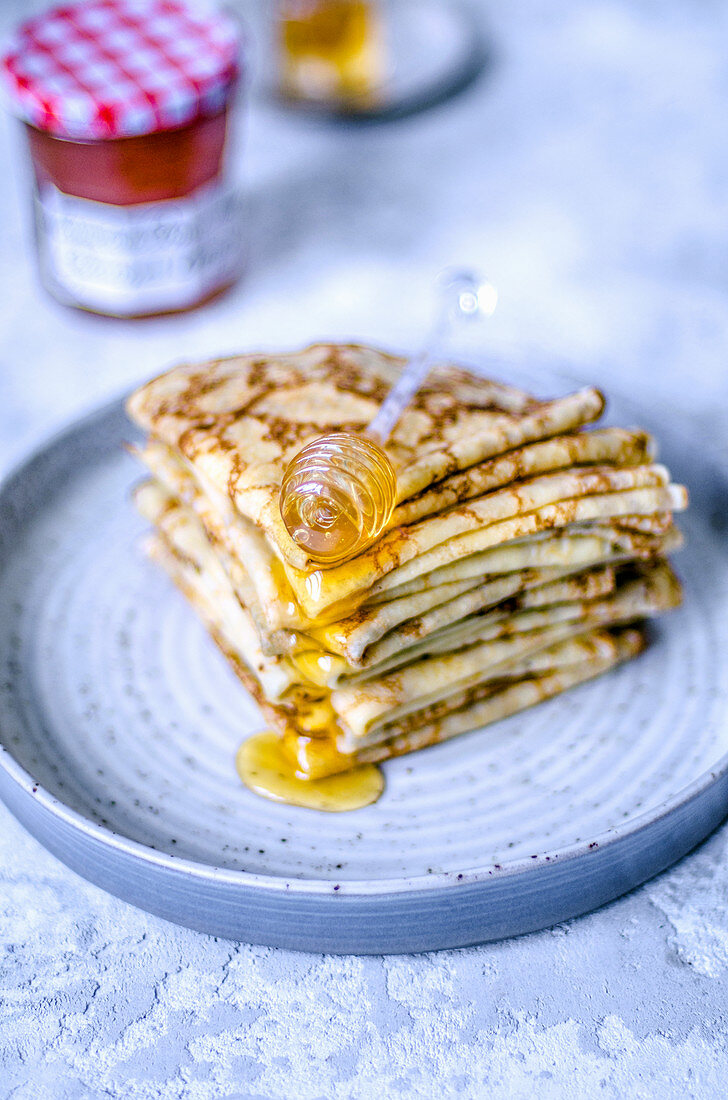 A stack of thin pancakes stacked in four layers with honey and a honey spoon