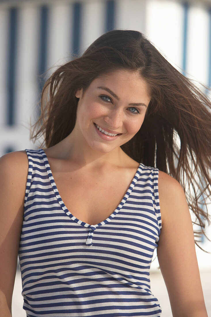 A young brunette woman on a beach wearing a blue-and-white striped top