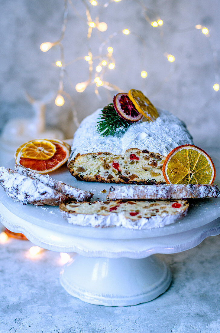 Christmas Stollen on a white stand decorated with dry slices of orange and garland