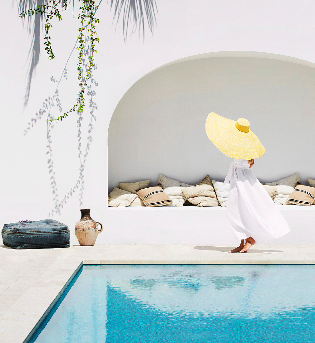 Frau mit Hut in weißem Kleid am Pool