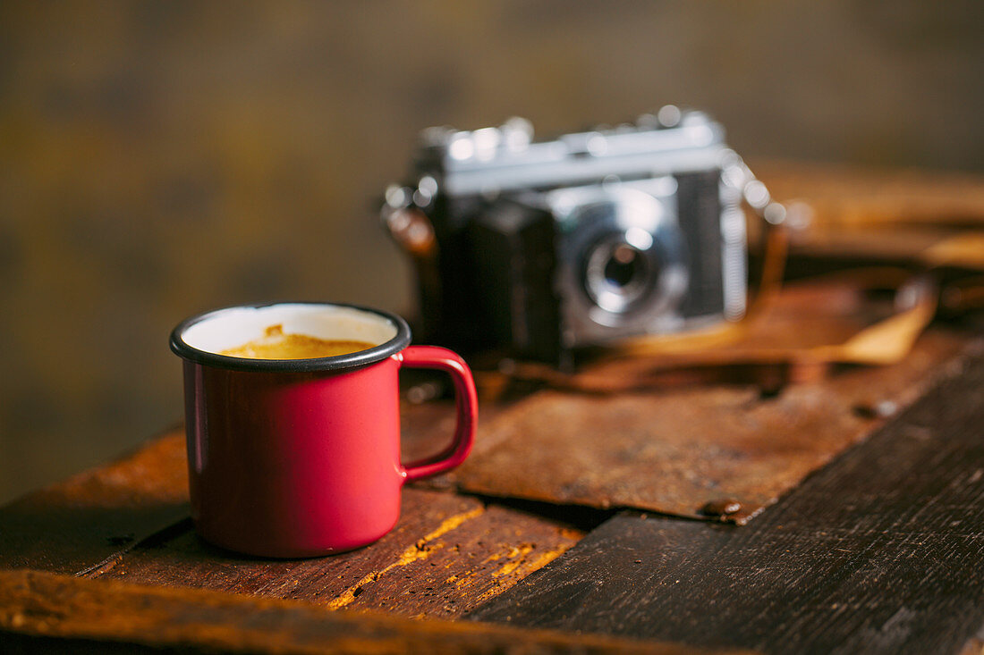 Kaffee in einer Emailtasse und Fotoapparat auf rustikalem Untergrund