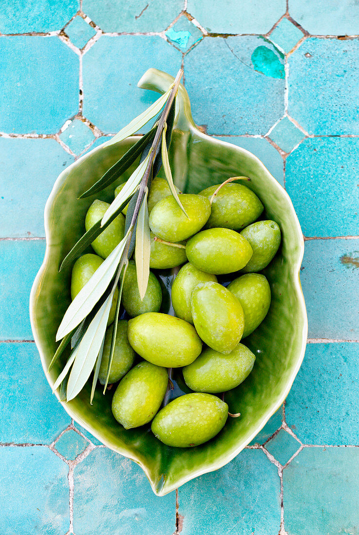 Green olives with a branch in a ceramic bowl