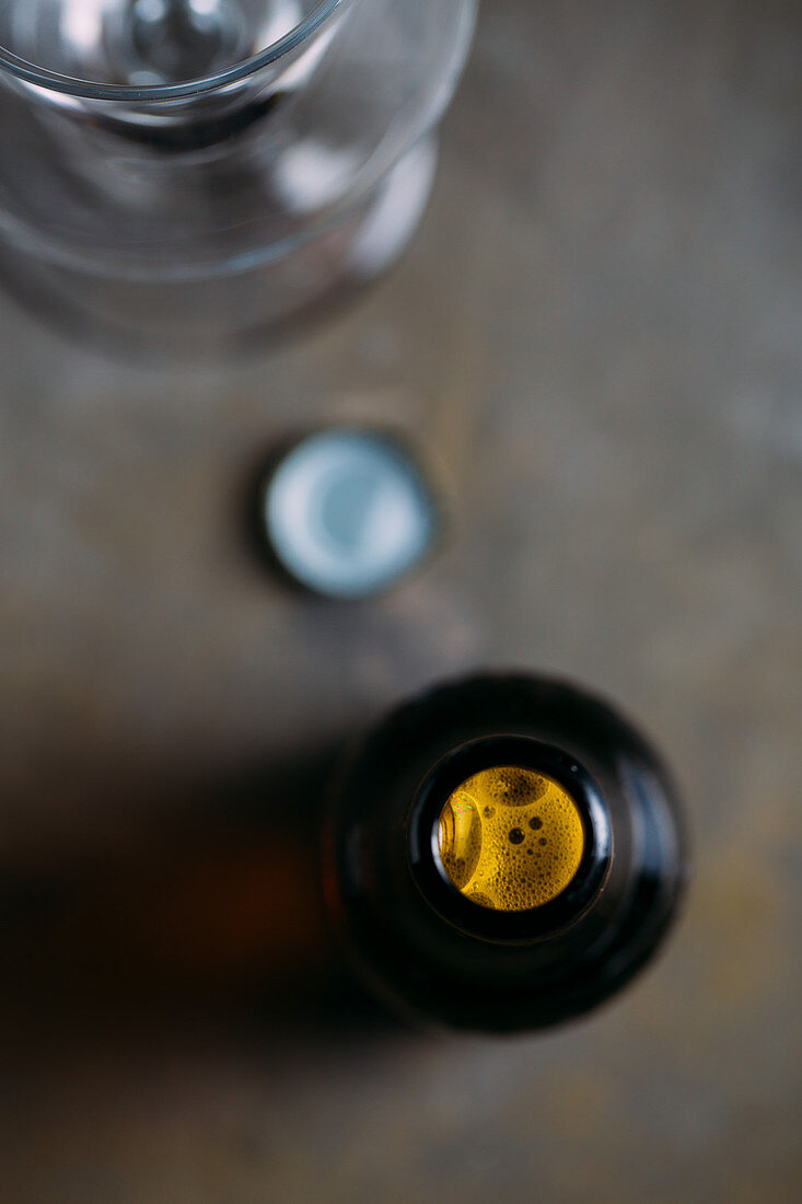 Geöffnete Bierflasche daneben Kronenkorken und Bierglas (Aufsicht)