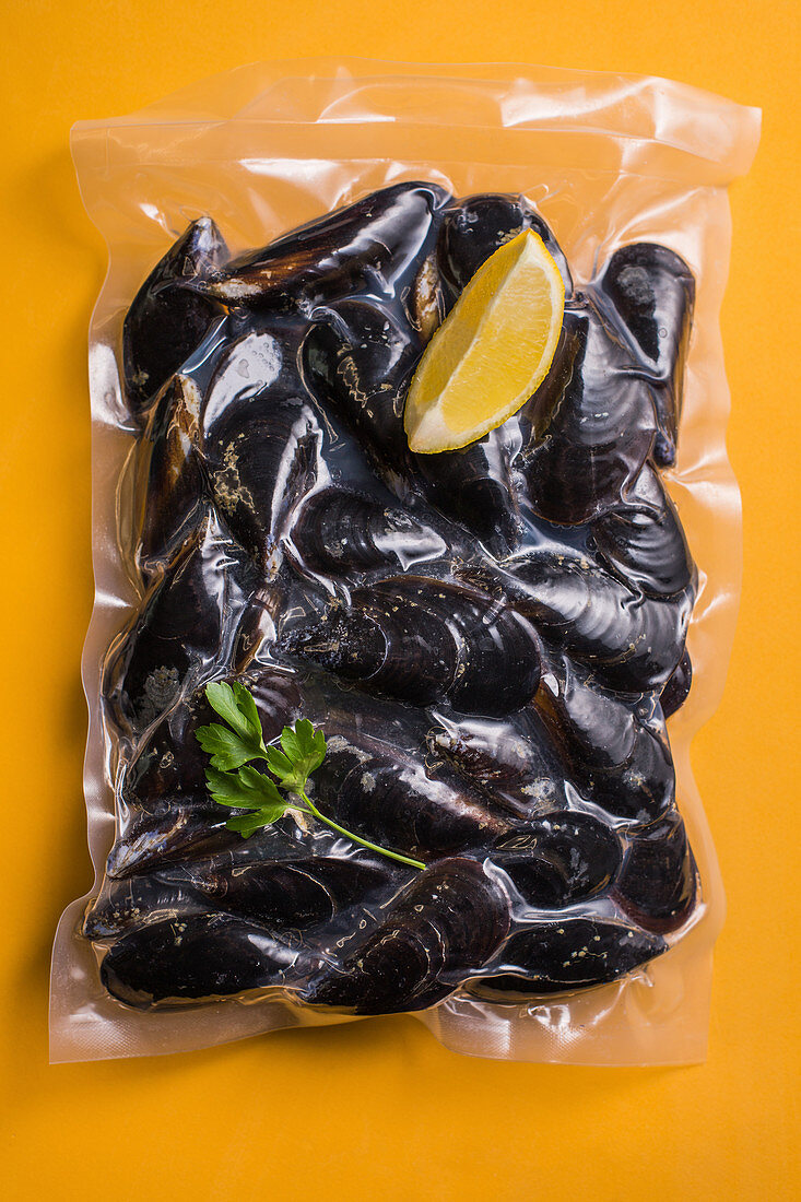 Cooked mussels sealed in plastic on a yellow surface